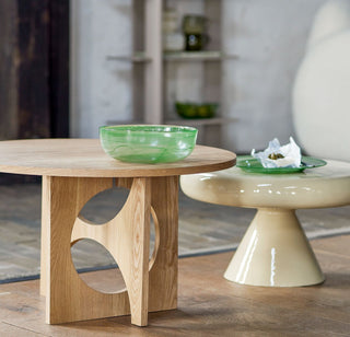 Twee ronde bijzettafels in lichte houtkleur en glanzend beige met groen glaswerk in een zithoek.