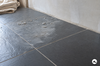 Cementsluier en opgedroogde cementspatten op een donkere leisteenvloer