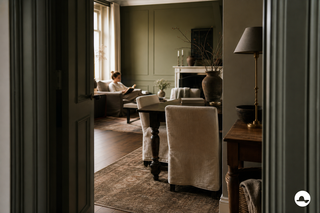 Interior clásico atemporal con paneles verde oliva, madera oscura y sillas de lino