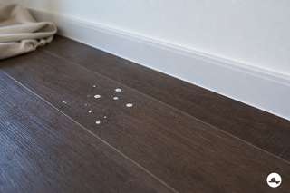Small dry white paint splashes on a dark wood-effect PVC floor