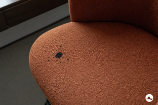 Black ink stain with small splashes on a rust-coloured bouclé chair