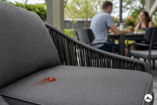 Rode ketchupvlek op een donker buitenkussen bij de eettafel