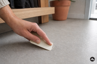 Lijmresten voorzichtig verwijderen van een lichtgrijze PVC-vloer met een kunststof pasje