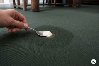 Mayonaisevlek met vetkring op een bosgroen vloerkleed voorzichtig opscheppen