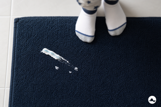 Witte tandpastavlek op een donkere badmat in een lichte badkamer