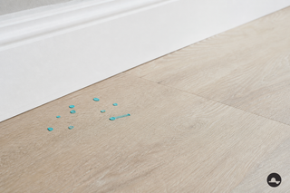 Gotas secas de pintura turquesa sobre un suelo de PVC claro junto al rodapié