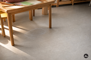 Melkachtige wateroplosbare lijmfilm op een lichtgrijze PVC-vloer onder een knutseltafel