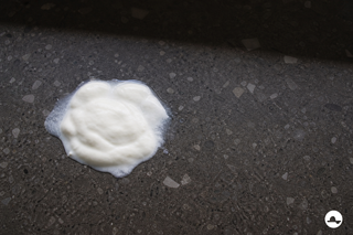 Dikke yoghurtvlek met matte vochtrand op een donkere terrazzovloer