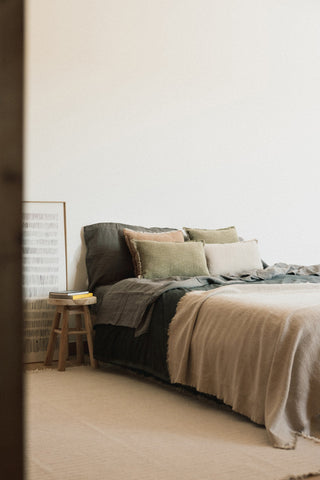 Naturel Handloom-plaid over een bed met groene en lichte kussens.