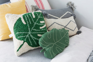 Sierkussens in groen, geel en naturel, met een Monstera-bladmotief vooraan.