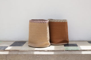 Twee gevlochten textielmanden in naturel en terracotta op een tegelvloer.