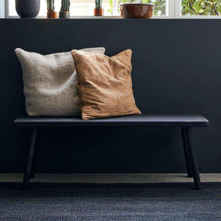 Zwarte bank met twee kussens in beige en bruin voor een donkere wand