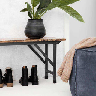 Houten bank met zwart metalen onderstel, plant en laarzen in een interieur