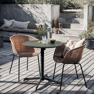 Groene ronde buitentafel met glazen en hapjes tussen twee gevlochten stoelen op een houten terras