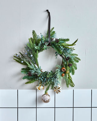 Deco kunstkrans Ø 53 cm aan een lichte binnenwand, gestyled met losse kerstballen