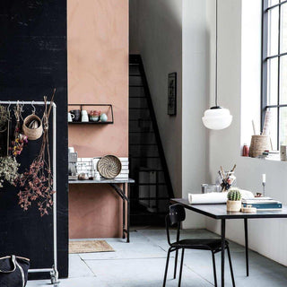 Stijlvolle woonkamer met zwarte tafel, stoel en hanglamp, roze muur en natuurlijke accessoires