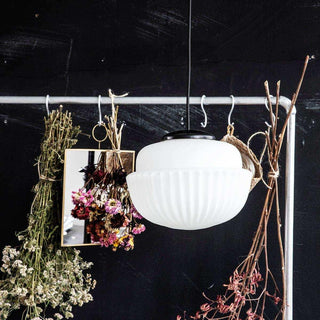 Witte hanglamp met geribbelde glazen kap en zwarte fitting, omringd door gedroogde bloemen en takken