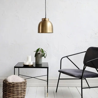 Gouden hanglamp boven zwarte bijzettafel met plant en kaarsen, naast donkere fauteuil in minimalistische woonkamer