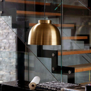 Gouden hanglamp met metalen kap boven donkere tafel in moderne woonkamer