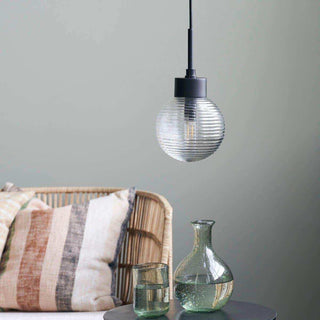 Gaia hanglamp met geribbelde glazen bol boven een bijzettafel naast een gevlochten stoel