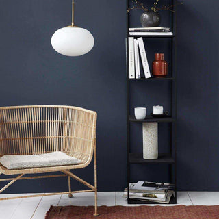 Rieten fauteuil met kussen naast zwarte boekenkast en hanglamp in donkerblauwe woonkamer