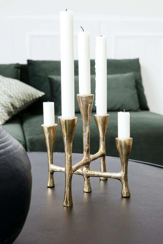 Gouden kandelaar met witte kaarsen op donkere tafel, stijlvol woonaccessoire