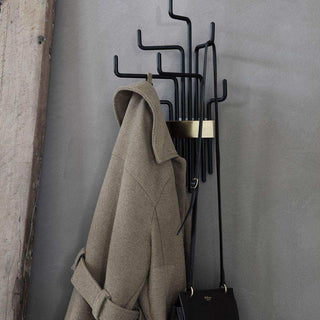 Zwart metalen kapstok met gouden accent, hangend met beige jas en zwarte tas