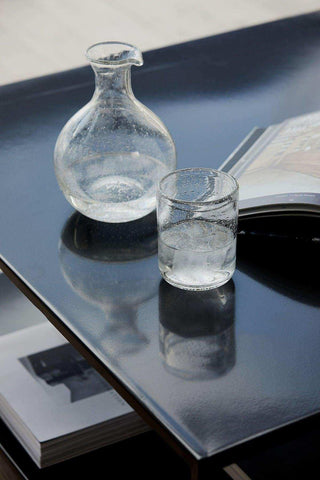 Glazen waterkaraf en drinkglas met luchtbelletjes op een donkere tafel naast een open boek