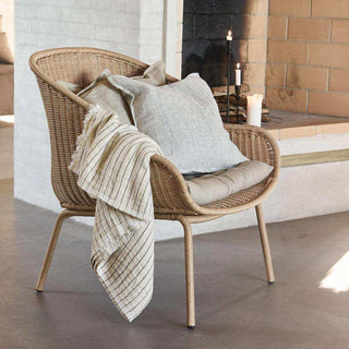 Hapur lounge stoel met zitkussen, sierkussens en plaid naast een haard met brandende kaarsen