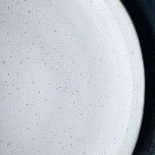 Detail van de witte, subtiel gespikkelde afwerking en licht opstaande rand van het lunchbord