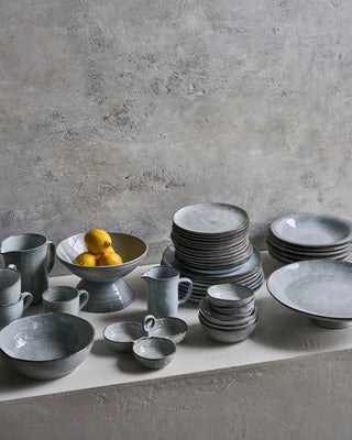 Assortiment grijs gespikkeld servies met stapels borden, kommen, kannen en een schaal met citroenen