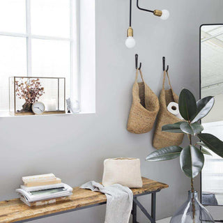 Rieten manden aan muurhaken in moderne woonkamer met houten tafel en plant