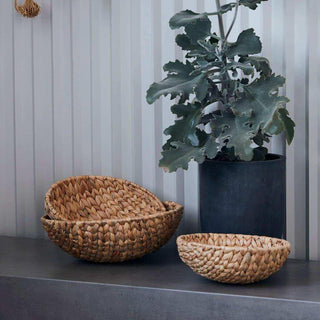 Geweven rieten manden in natuurlijke kleur, ideaal als woonaccessoire naast een plant in een donkere pot