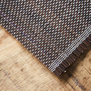 Detail van de bruine placemat met witte en paarse weefdraden op een houten tafel