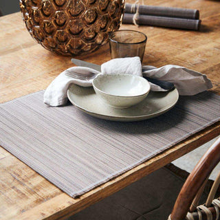 Bruine geweven placemat op een houten tafel, gedekt met servies, bestek en een servet