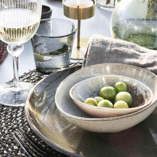 Grijze keramische schalen met groene olijven op tafel, bij wijnglas en kaarsenhouder