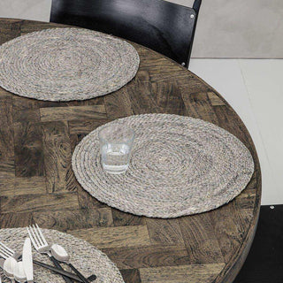 Ronde gevlochten placemats op houten tafel met glas en bestek