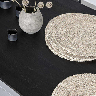 Ronde gevlochten placemats van riet op zwarte tafel met grijze vaas en kaarsen