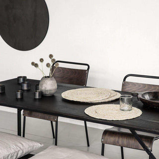 Ronde jute placemats op zwarte eettafel met houten stoelen en grijze vaas