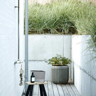 Geribbelde Concrete bloempot met plant naast een buitendouche op een houten vlonder