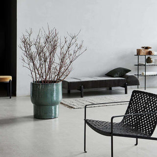 Terra bloempot met kale takken in een modern interieur met ligbank en stoel