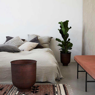 Grote donkerrode Vig plantenpot bij een bed, met kleinere pot en kamerplant op de achtergrond