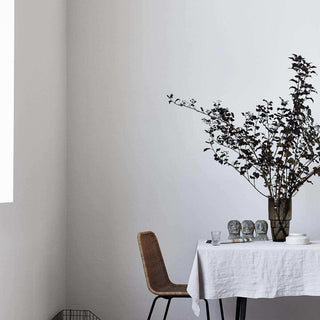 Stoel Haput naast een tafel met wit kleed, decoraties en een hoge vaas met takken
