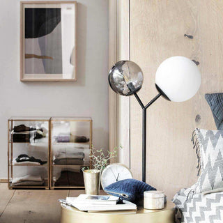 Zwarte Twice lamp met twee ronde glazen kappen naast een ronde gouden tafel in een interieur