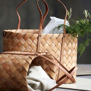 Twee gevlochten Beach tassen met lange hengsels, gevuld met textiel en groene takken