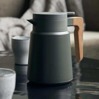 Thermoskan Cole met schenktuit en houten handvat op tafel, met bekers op de achtergrond