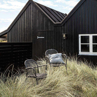 Twee Brea tuinstoelen, waarvan één met kussen, tussen hoog siergras bij een houten huis