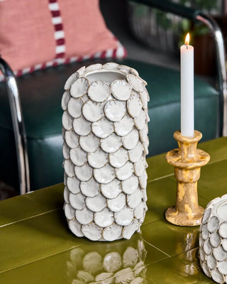Witte vaas met ronde schijfjes naast een gouden kandelaar op een groene tafel