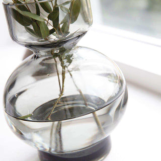 Detail van de ronde, grijs getinte glazen vaas met groene takken en water