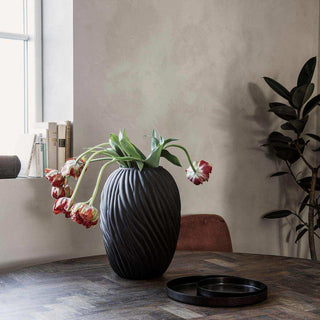 Donkere vaas Noa met golvend reliëf en hangende tulpen op een tafel bij het raam